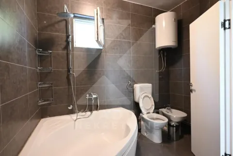 Bathroom with a bathtub, toilet, bidet, and water heater tiled in dark tiles. - image 24