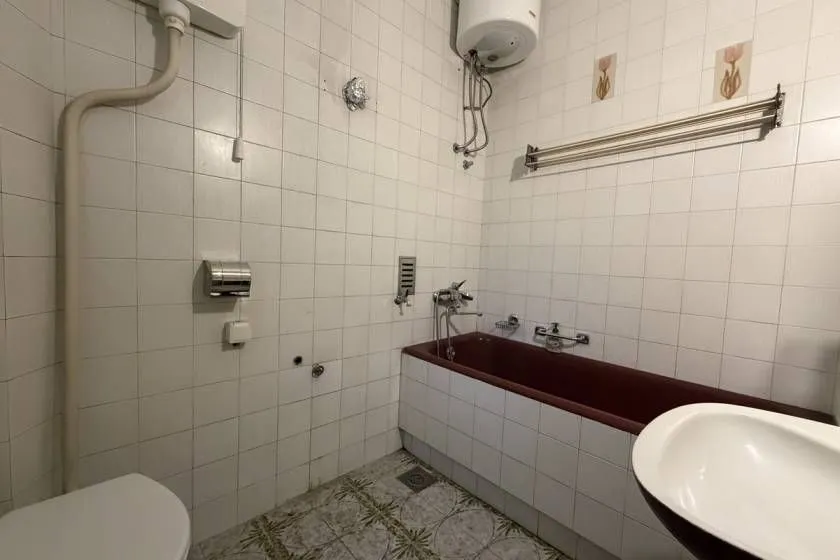 Smaller bathroom with a bathtub, washbasin and a water heater on the wall.