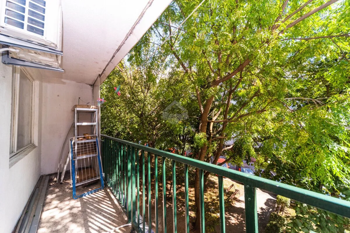 Balkon sa zelenim ogradama i pogledom na drveće.