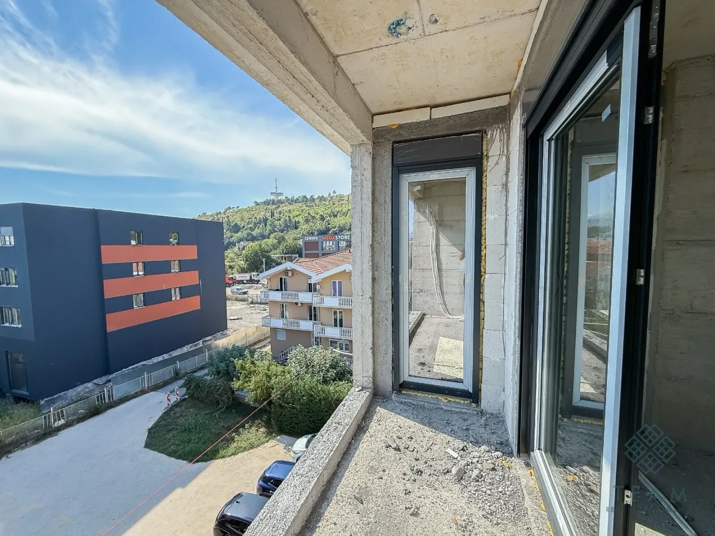 Nezavršeni balkon u izgradnji sa pogledom na okolne zgrade i pejzaž.