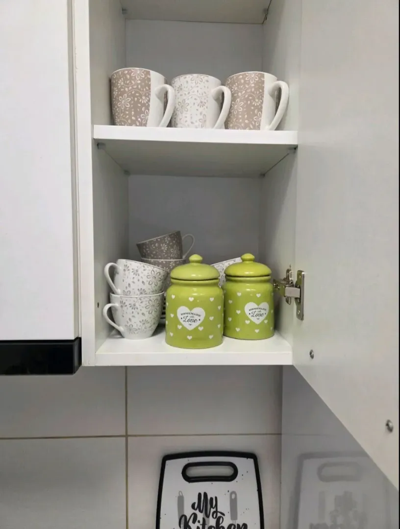 Otvoreni kuhinjski element sa šoljama i teglama za začine.