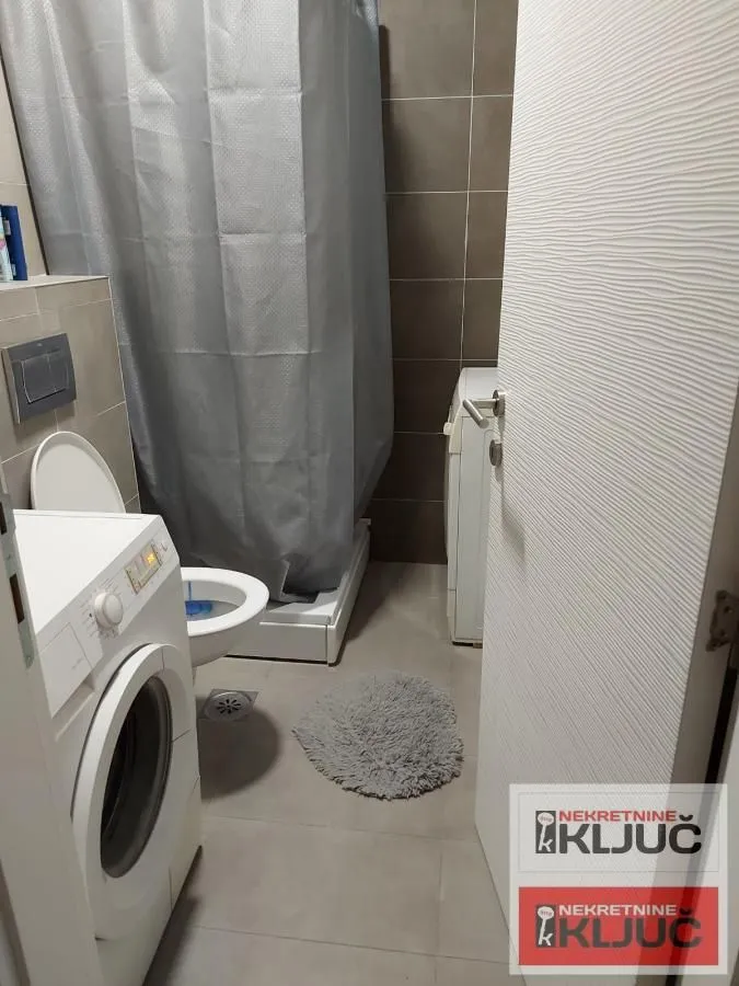 Manje kupatilo sa tuš kabinom, WC šoljom i veš mašinom.