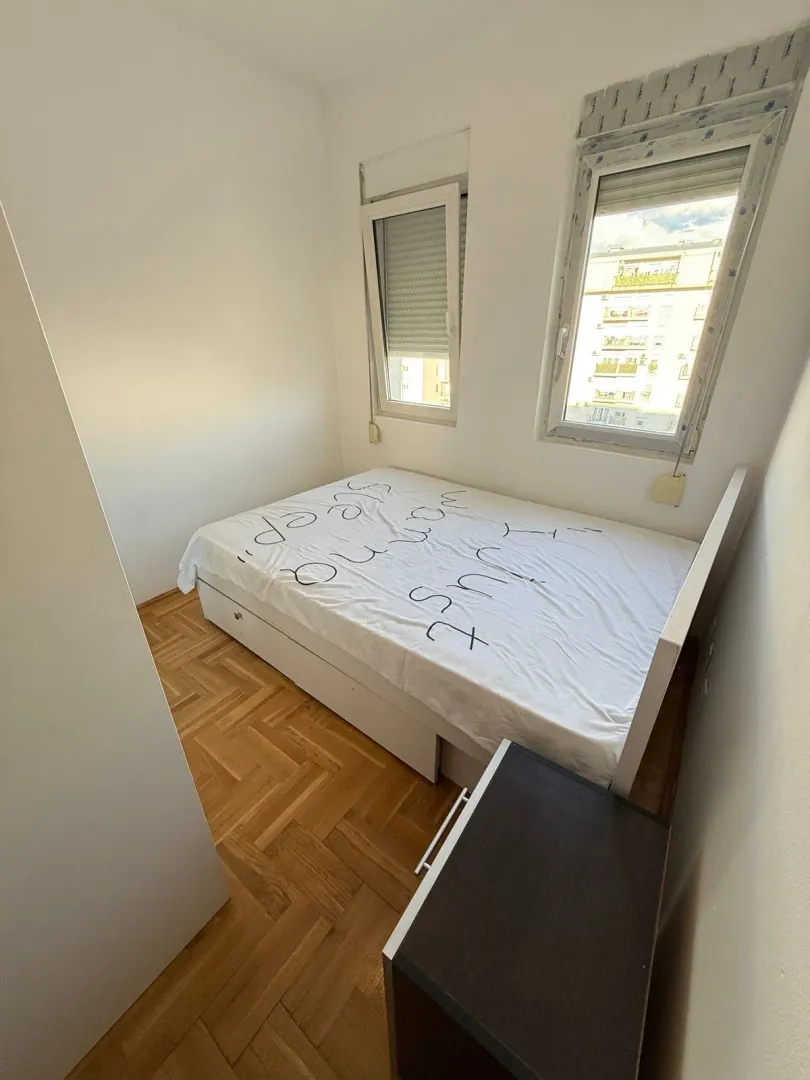 Small bedroom with a double bed, parquet flooring, and two windows.