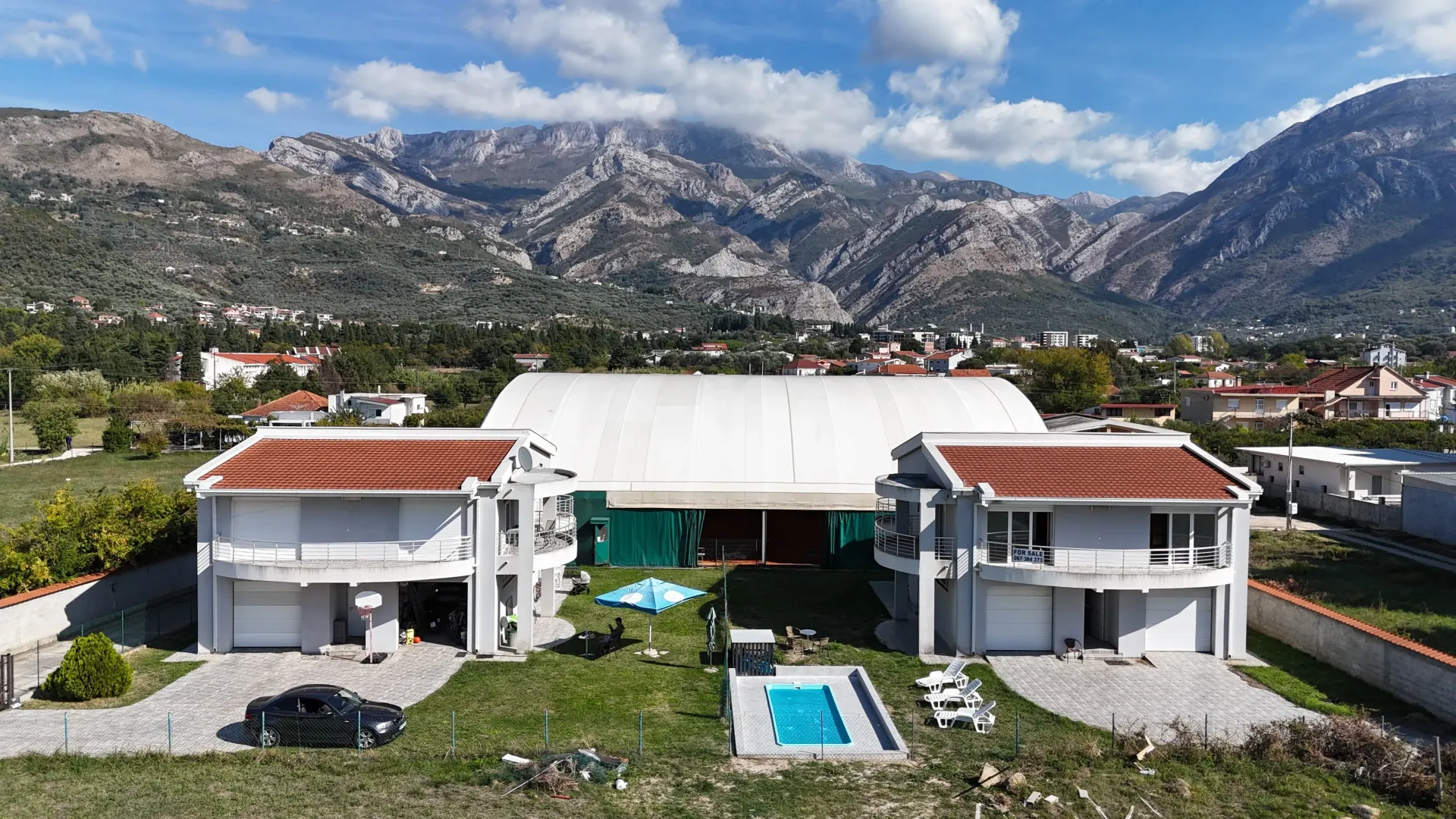 Pogled iz vazduha na dvije kuće sa bazenom i planinskim pejzažem u pozadini.