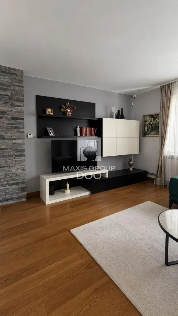 Dnevna soba sa modernim nameštajem za televizor i zidom obloženim kamenom.