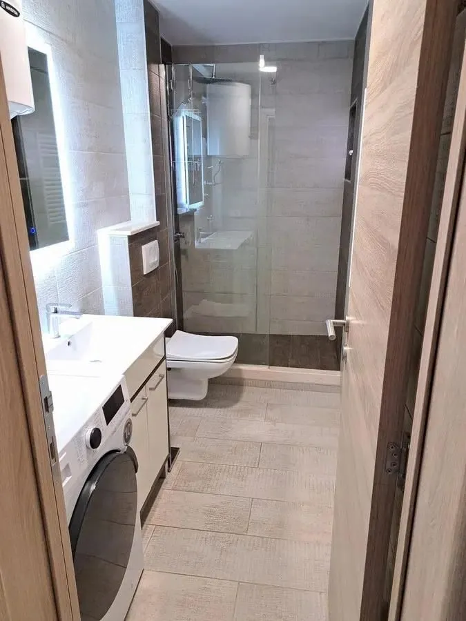 Moderne kupatilo sa tuš kabinom, umivaonikom i veš mašinom.