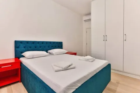 Spavaća soba sa bračnim krevetom, crvenim noćnim stolićima i bijelim garderoberom. - image 7