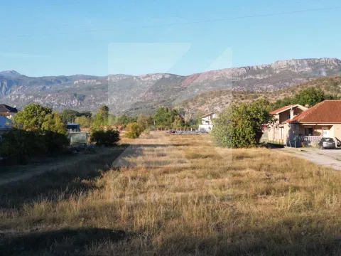 Pogled na plac sa travnatom površinom i okolnim kućama i brdima u pozadini. - image 2