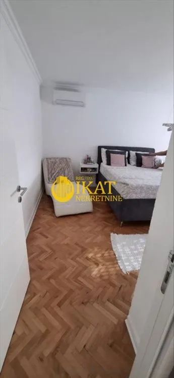 Spavaća soba sa bračnim krevetom, foteljom i parketom na podu.