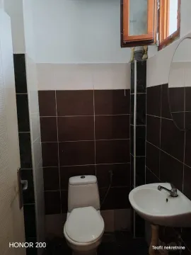 Manje kupatilo obloženo tamnim i svetlim pločicama sa toaletom i umivaonikom. - image 12