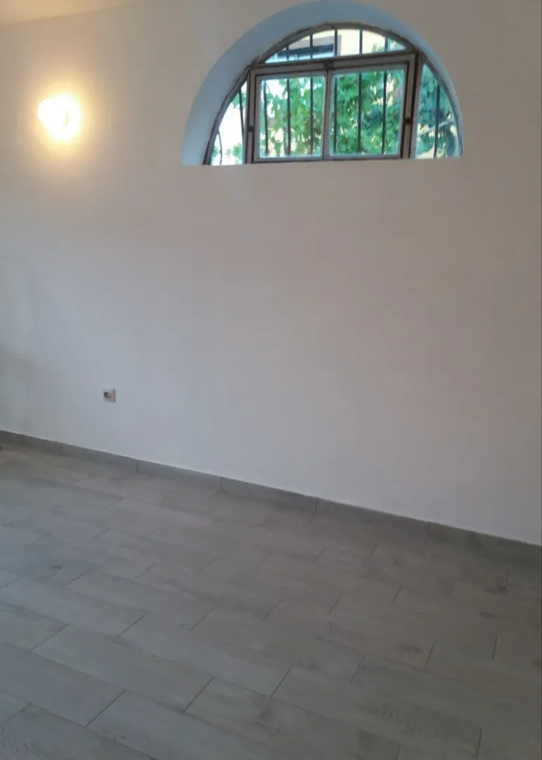 Empty room with white walls, grey tiled floor, and an arched window.