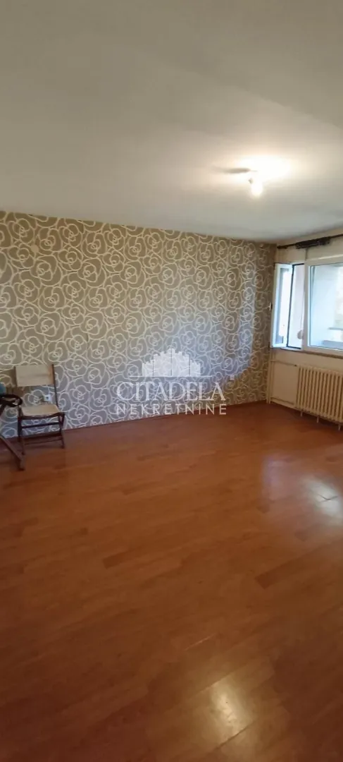 Prazna soba sa drvenim podom i dekorativnim tapetama na zidu.
