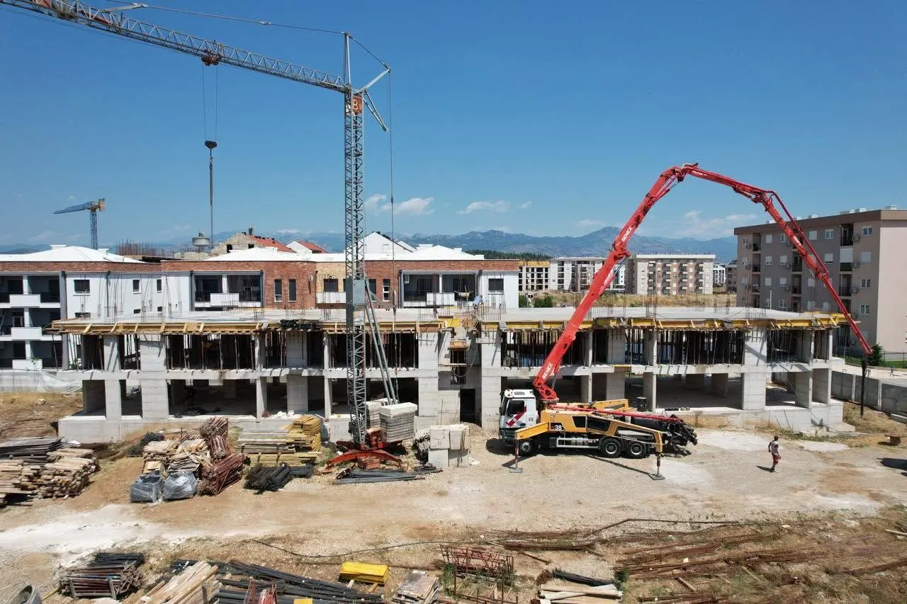 Pogled iz vazduha na gradilište stambenog objekta u izgradnji sa građevinskom mehanizacijom.