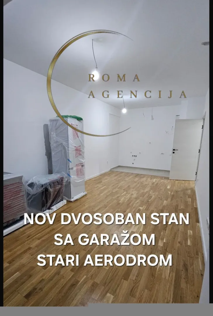 Prazna prostorija sa parketom i spakovanom kuhinjom.