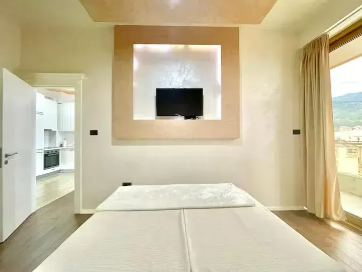 Prostrana spavaća soba sa bračnim krevetom, TV-om na zidu i pogledom na terasu.