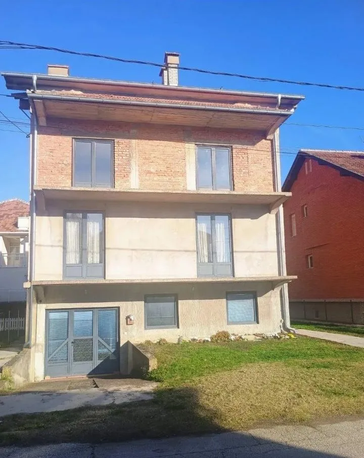 Prednja strana višespratne kuće sa balkonima i travnjakom.