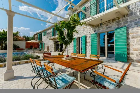 Terrace with a wooden table and chairs in front of a stone house with a swimming pool. - image 2