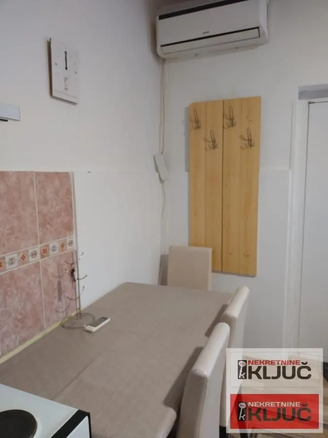 Manja trpezarija sa stolom, stolicama i klima uređajem na zidu.