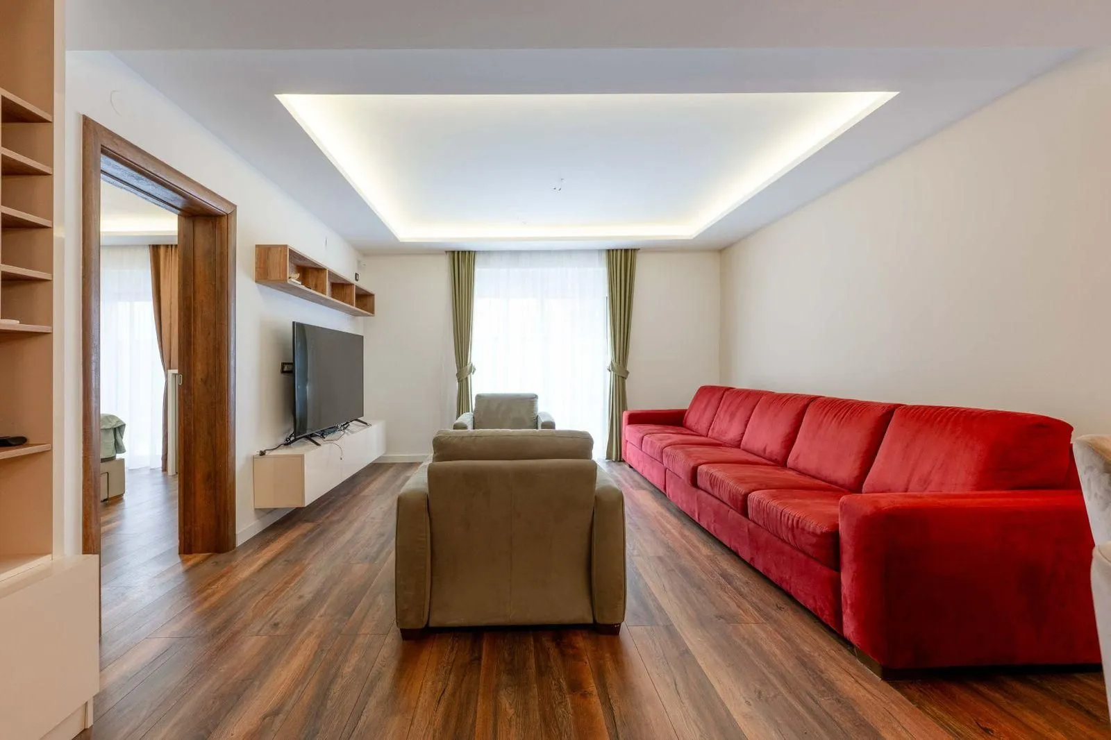 Prostrana dnevna soba sa velikom crvenom garniturom i TV-om.