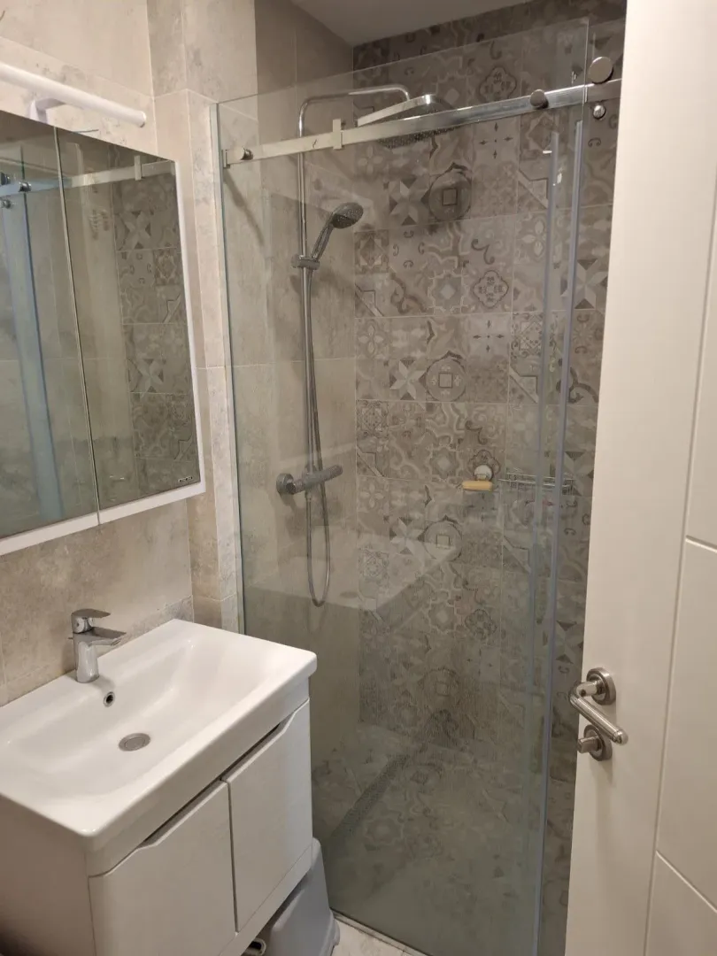 Moderne kupatilo sa tuš kabinom, umivaonikom i ogledalom.