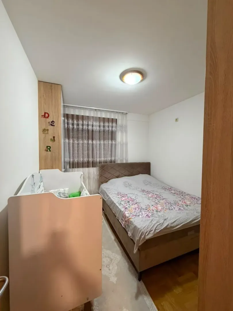 Uređena spavaća soba sa bračnim krevetom i dječijim krevetcem.
