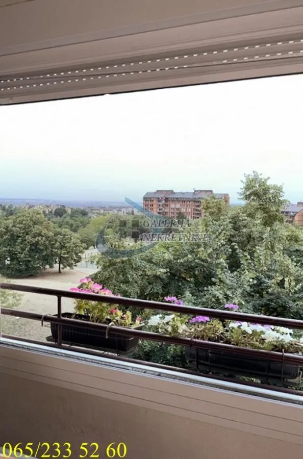 Pogled sa prozora na okolno zelenilo i zgrade.