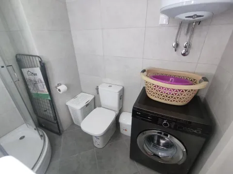 Bright bathroom with a shower cabin, toilet, and a washing machine. - image 12