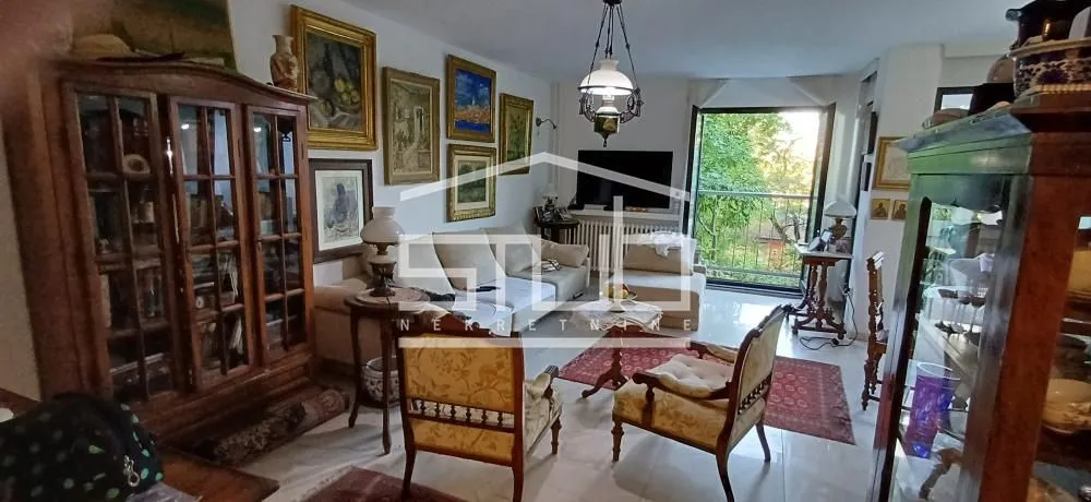 Dnevna soba sa garniturom, stilskim nameštajem i umetničkim slikama na zidu.