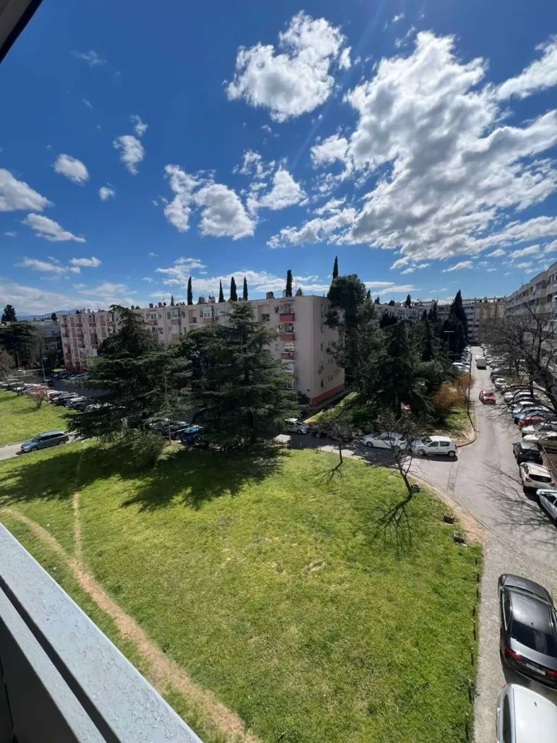 View from the window overlooking surrounding buildings, green areas, and parked vehicles.