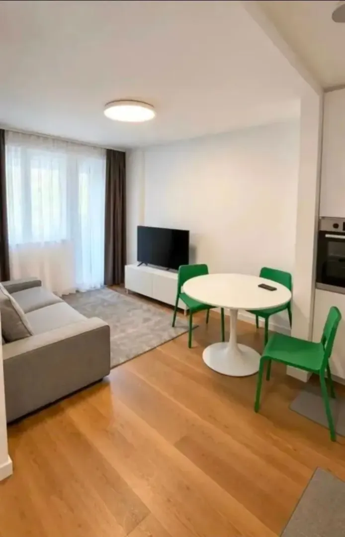 Living room with a sofa, TV, and dining table with green chairs.