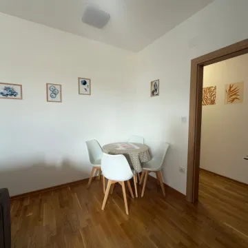 Manji trpezarijski sto sa četiri bijele stolice u uglu svijetle prostorije. - image 7