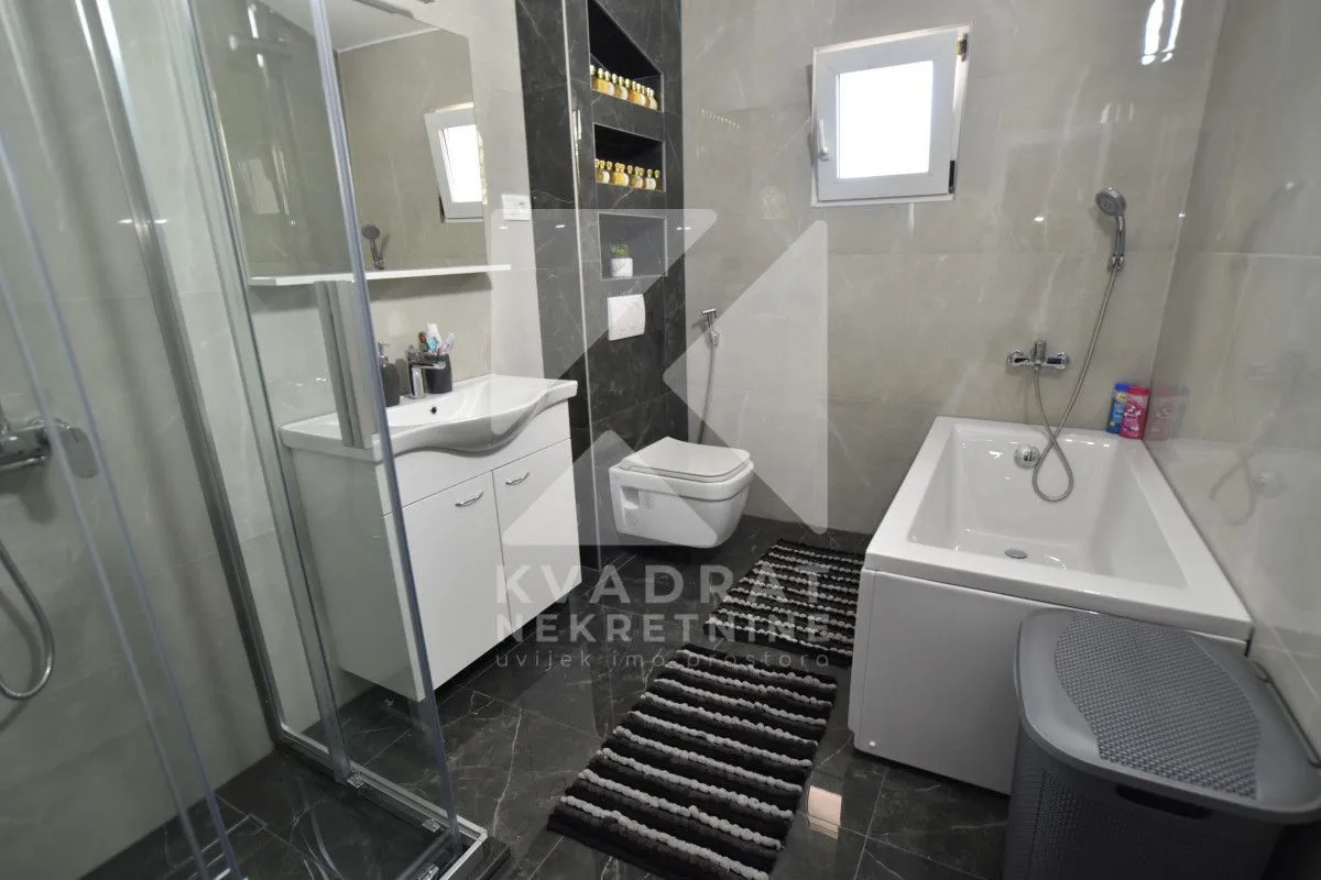 A modernly equipped bathroom with a shower cabin, bathtub, sink, and wall-hung toilet.