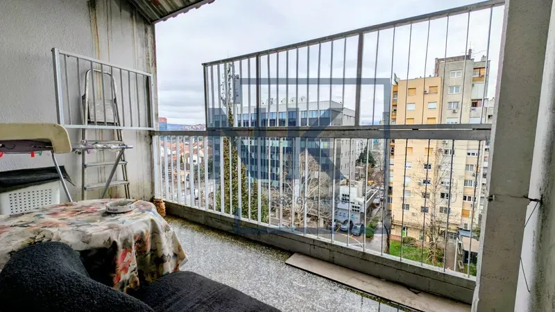 Covered balcony with railing and a view of surrounding buildings.