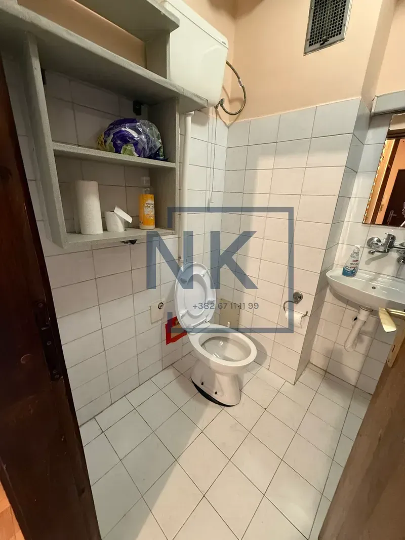 Small bathroom with white tiles, toilet, washbasin, and storage shelves.