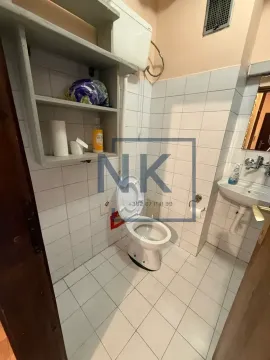 Small bathroom with white tiles, toilet, washbasin, and storage shelves. - image 11