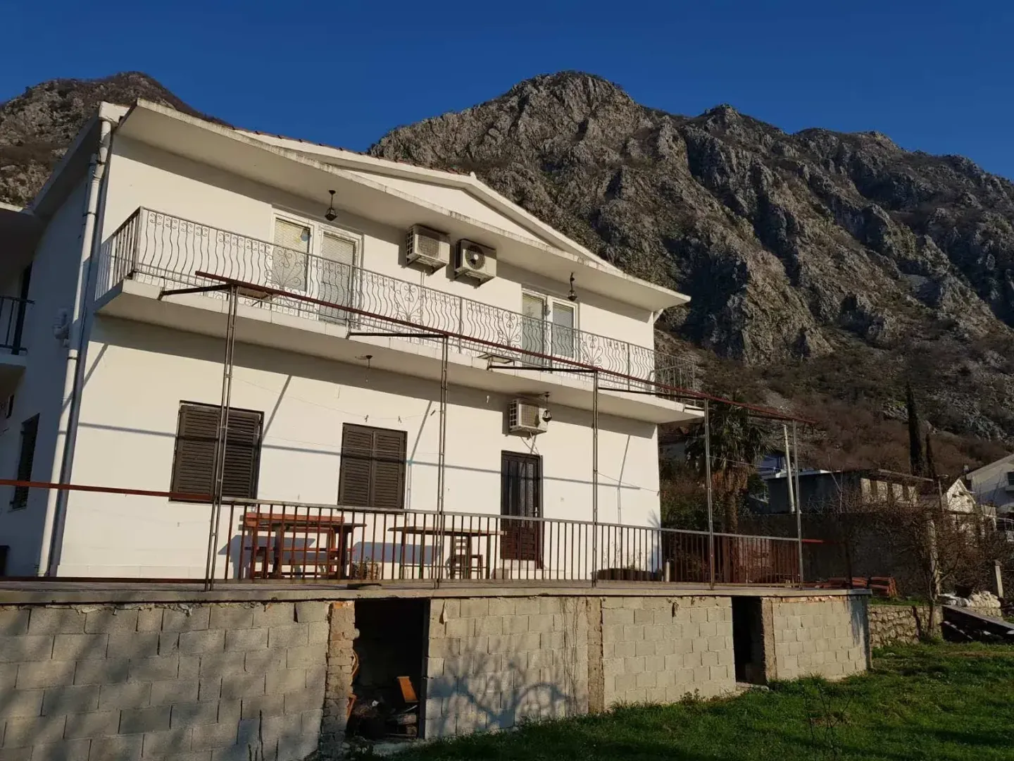 Exterior view of a two-story house with a terrace and mountain landscape in the background.