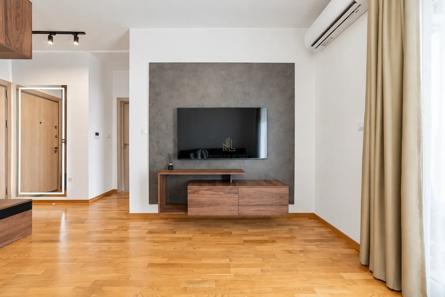 Dnevni boravak sa drvenim podom, TV komodom i montiranim klima uređajem.