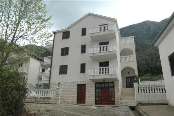 Pogled na spoljašnjost višespratne kuće sa bijelom fasadom i balkonima.