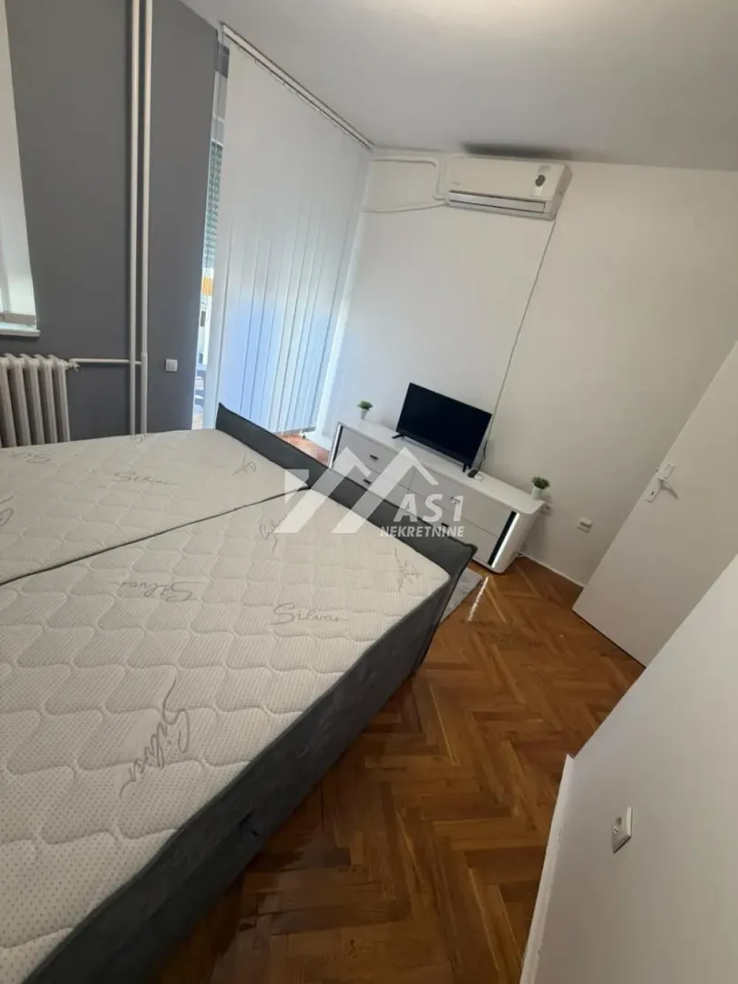 Spavaća soba sa bračnim krevetom, TV komodom i klima uređajem.