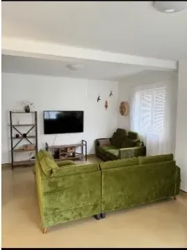 Living room with a green sectional sofa, TV, and shelves. - image 2