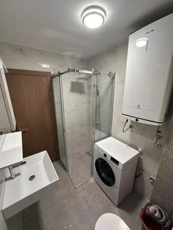 Moderno opremljeno kupatilo sa tuš kabinom, umivaonikom i veš mašinom.