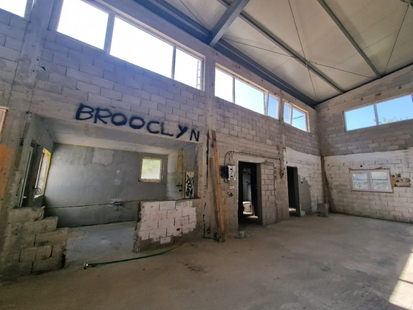 Unutrašnjost nedovršenog objekta sa betonskim blokovima i velikim prozorima.