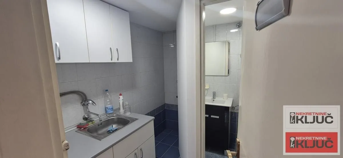 Manja kuhinja sa sudoperom i visećim elementima i pogledom na kupatilo.