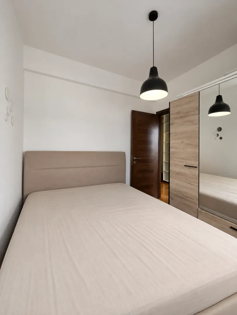 Moderna spavaća soba sa bračnim krevetom, garderoberom sa ogledalom i visećom lampom.