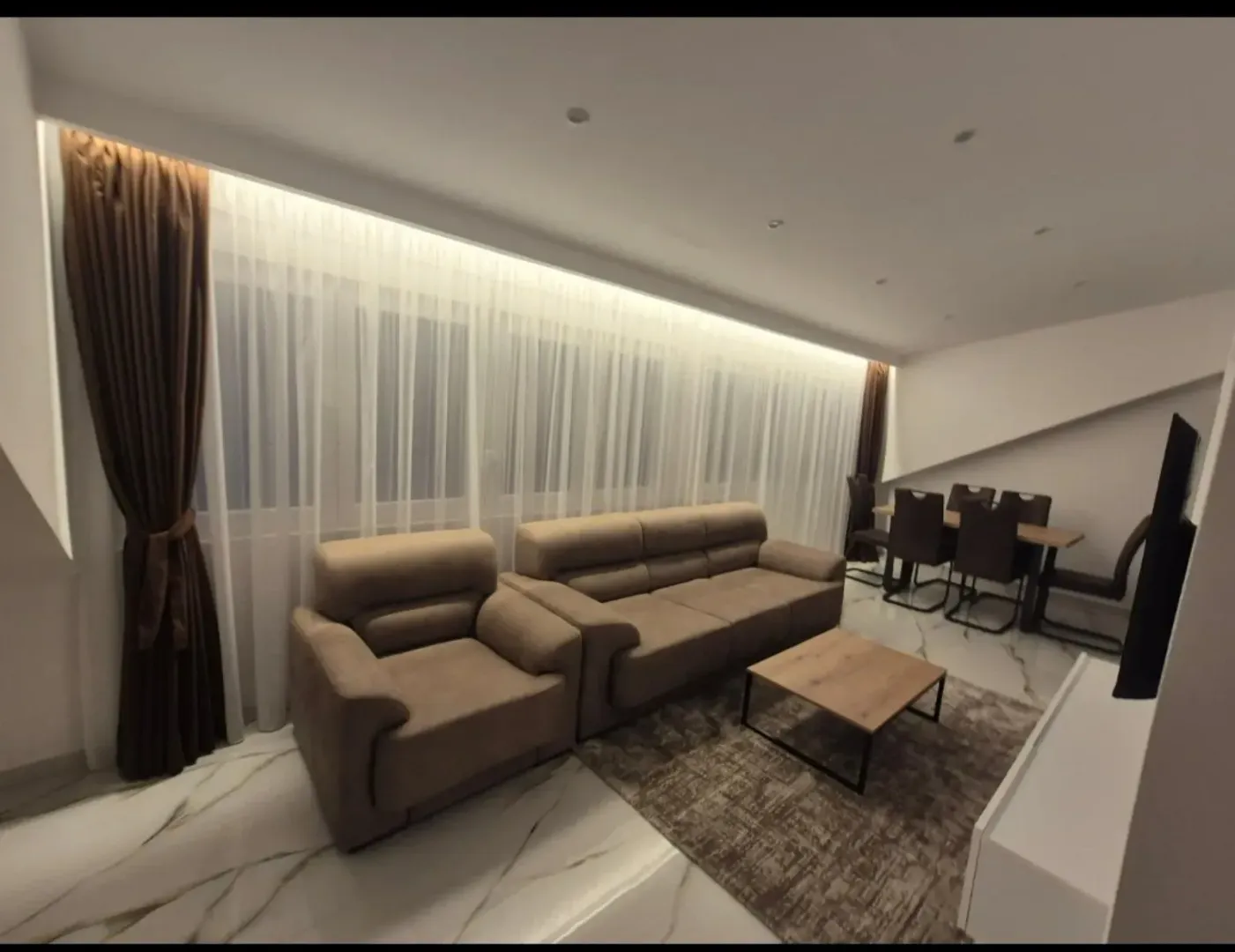 Living room with a sofa set, coffee table, and dining area in the background.