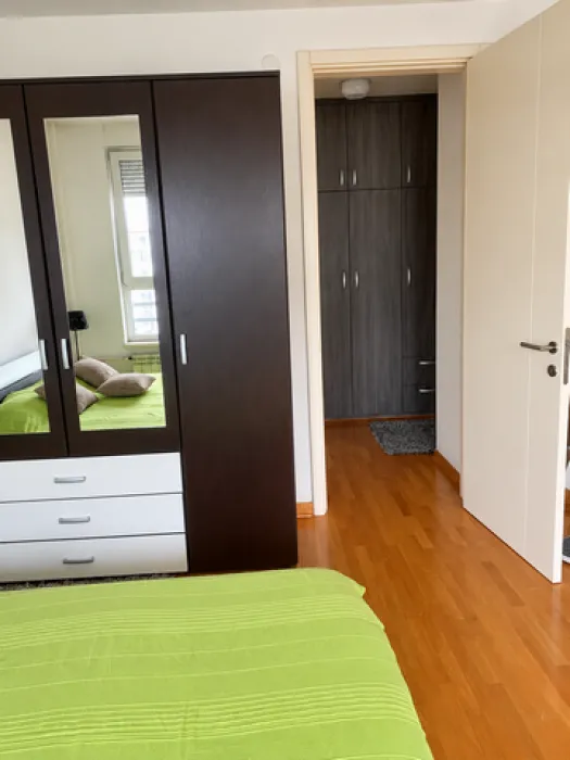 Bedroom with a large double bed, wardrobe, and a view into the hallway leading to another room.