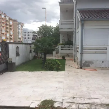 Popločano dvorište kuće sa travnjakom i malom palmom ispred fasade. - image 19