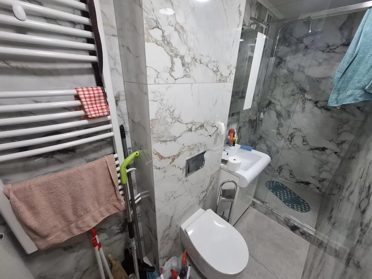 Moderno kupatilo sa tuš kabinom, umivaonikom i wc šoljom obloženo mermernim pločicama.
