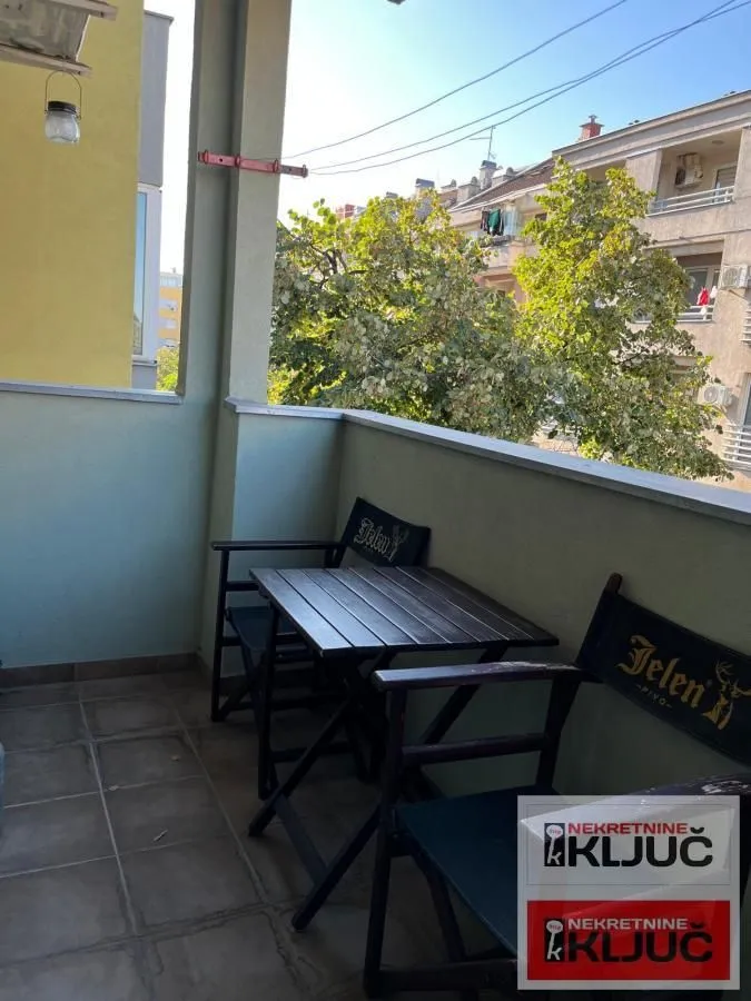 Covered balcony with seating set and view of surrounding buildings and trees.