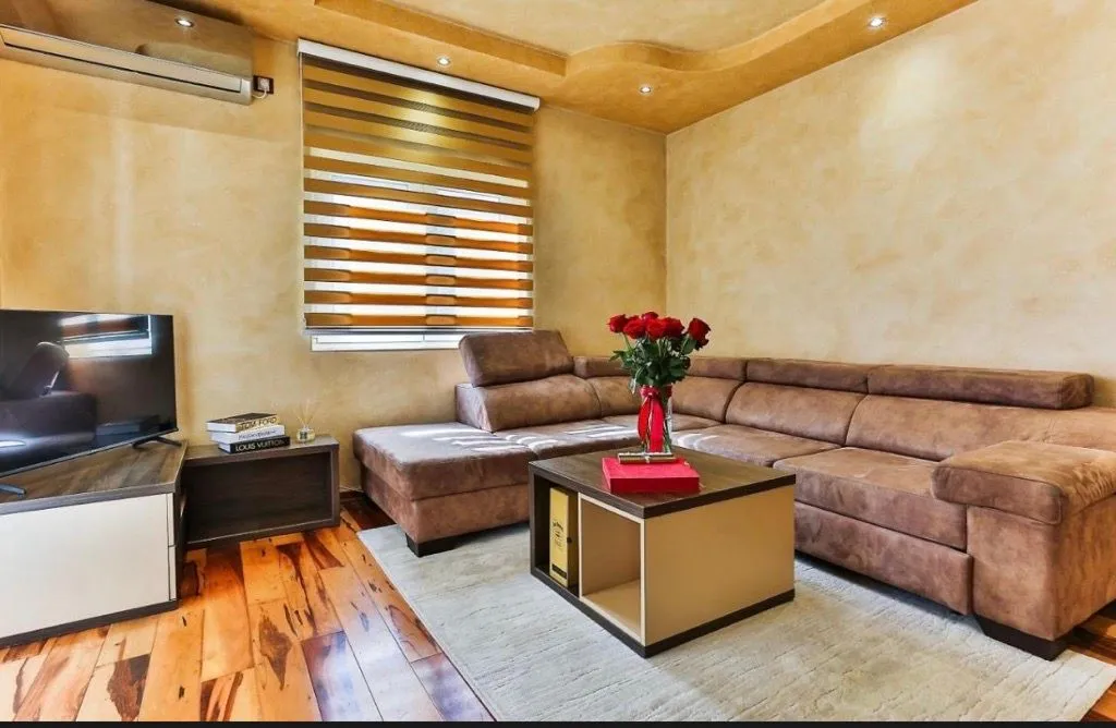 Living room with a corner sofa, coffee table, television, and window with blinds.